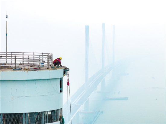 建設(shè)者在塔柱上施工，遠處“海上長龍”若隱若現(xiàn)。